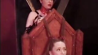 Mature mistress in a leather suit hangs clothespins on her young slave's shaved pussy in the basement