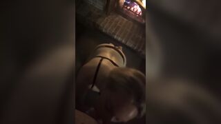 Golden-haired in ebony belt gives oral job by a fire