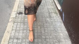 youthful female hippie is walking barefoot in public street