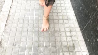 youthful female hippie is walking barefoot in public street