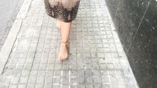 youthful female hippie is walking barefoot in public street