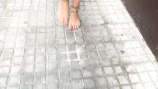 youthful female hippie is walking barefoot in public street