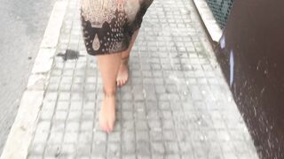 youthful female hippie is walking barefoot in public street